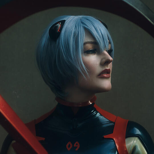 AmieDD dressed as Rei Ayanami from Neon Genesis Evangelion, wearing a sleek latex suit and sporting blue hair.